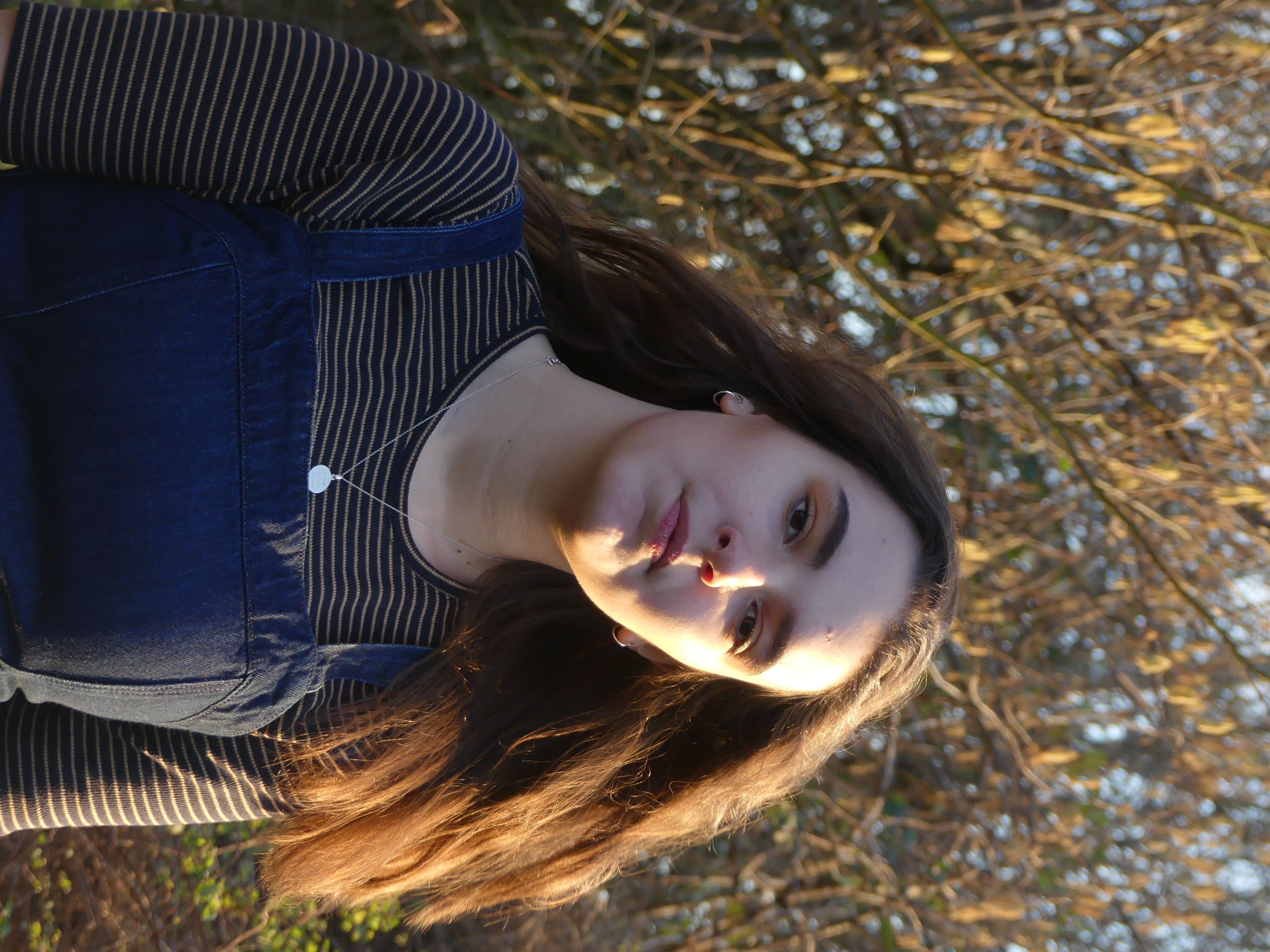 image of the model posed in sunlight against a backdrop of greenery
